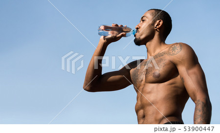 Muscular Afro Man Drinking Water After Workout Against Blue Sky 53900447