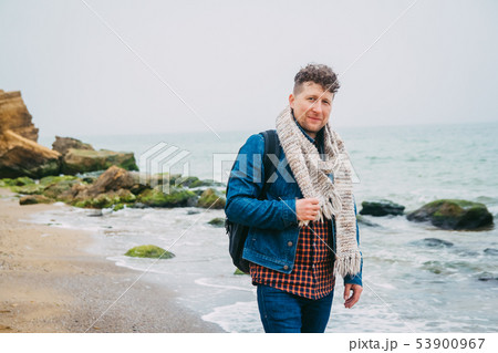 Traveler with a backpack standing near a beautiful sea with waves, a stylish hipster boy posing near 53900967
