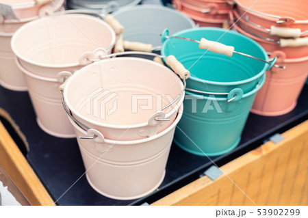 Various multicolored bright small ornamental metal buckets for sale on wooden table outdoors. Many Various multicolored bright small ornamental metal buckets for sale on wooden table outdoors. Many 53902299