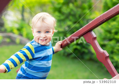 Portrait of cute mischievous caucasian blond baby boy holding wooden banister climbing staircase at 53902310