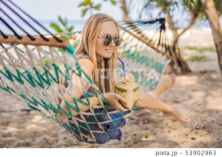 Young woman on the beach in a hammock with a drink Young woman on the beach in a hammock with a drink 53902963