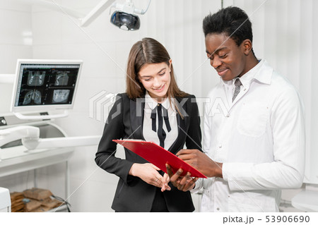 Young African male dentist makes a diagnosis and records recommendations. Woman patient at dental Young African male dentist makes a diagnosis and records recommendations. Woman patient at dental 53906690