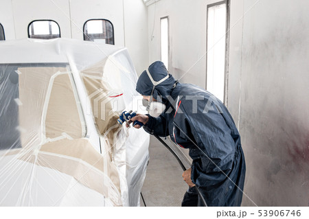 Car service station. Worker painting a white car in special garage, wearing costume and protective 53906746
