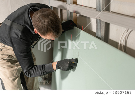 A man working Builder makes a marking on the drywall for electrical wiring. Metal drywall A man working Builder makes a marking on the drywall for electrical wiring. Metal drywall 53907165