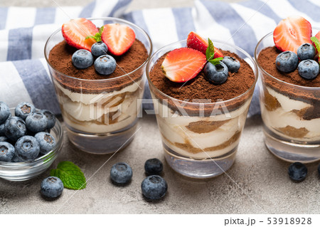 Classic tiramisu dessert with blueberries and strawberries in a glass on concrete background Classic tiramisu dessert with blueberries and strawberries in a glass on concrete background 53918928