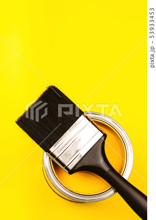 Brush with black handle on open can of paint on yellow background. 53933453
