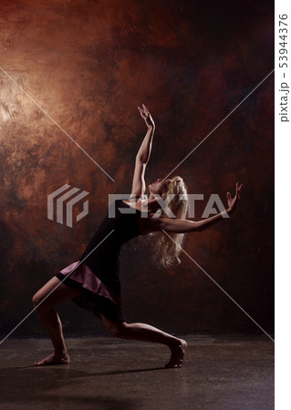 Full-length photo of young blonde dancer looking up in short black dress on brown background Full-length photo of young blonde dancer looking up in short black dress on brown background 53944376