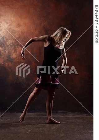 Full-length photo of dancing blonde in short black dress on brown background Full-length photo of dancing blonde in short black dress on brown background 53944378