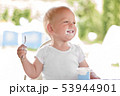 Smiling little blonde toddler boy eating delicious yogurt sitting outdoor 53944901