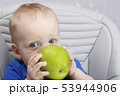 Cute baby 1,4 years old sitting on high children chair and eating green apple alone in white kitchen 53944906