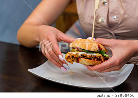 Hands of young woman holding burger in restaurant close 53968456