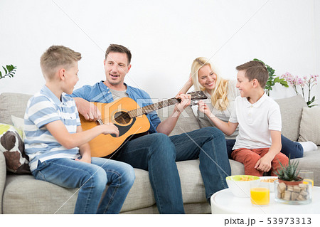 Happy caucasian family smiling, playing guitar and singing songs together at cosy modern home Happy caucasian family smiling, playing guitar and singing songs together at cosy modern home 53973313