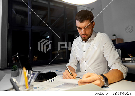 businessman with papers and laptop at night office 53984015