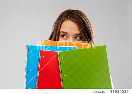 teenage student girl hiding behind notebooks 53984057