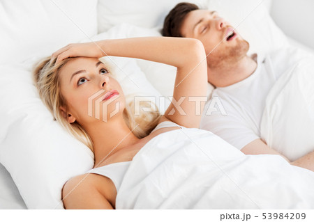 unhappy woman in bed with snoring sleeping man 53984209