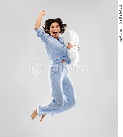 happy woman in blue pajama jumping with pillow 53986423