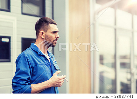 auto mechanic smoking cigarette at car workshop auto mechanic smoking cigarette at car workshop 53987741