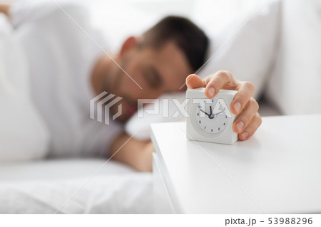 close up of man in bed reaching for alarm clock 53988296