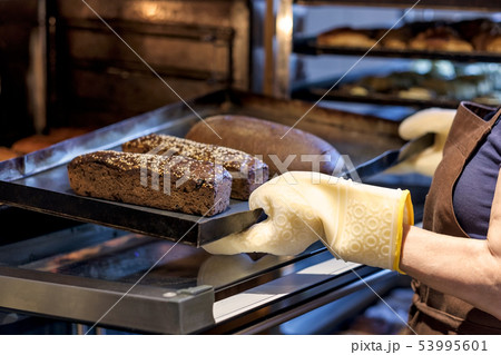 baker holding a tray with fresh bread taking it out of oven. baker holding a tray with fresh bread taking it out of oven. 53995601