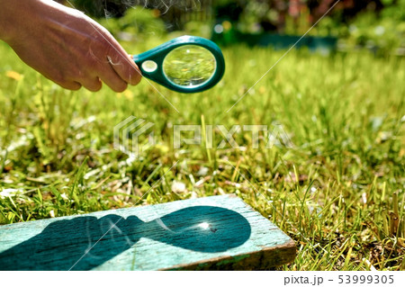 Man holding a magnifying glass making fire, focused on wood. 53999305