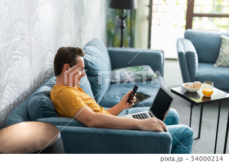 Adult man with smartphone sitting on sofa in room 54000214