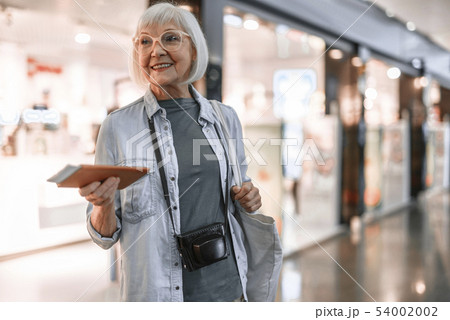 Smiling senior lady with bag staying at hall near shop 54002002