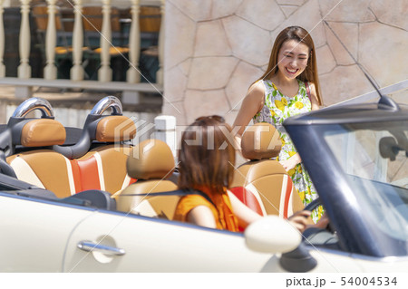 おしゃれな街に住む女友達に合わせて可愛い本革シートのオープンカーで迎えに来た花柄ワンピースを着た女性 54004534
