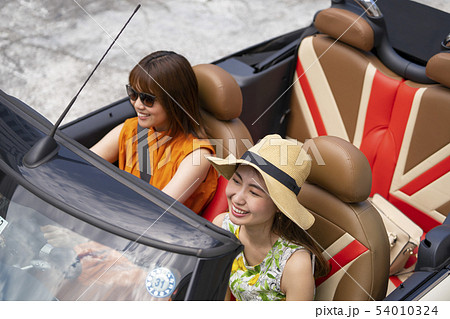 おしゃれなオープンカーに乗りセレブ感を醸し出すボタニカル柄のワンピースと麦わら帽子の女性真夏の女子旅の写真素材