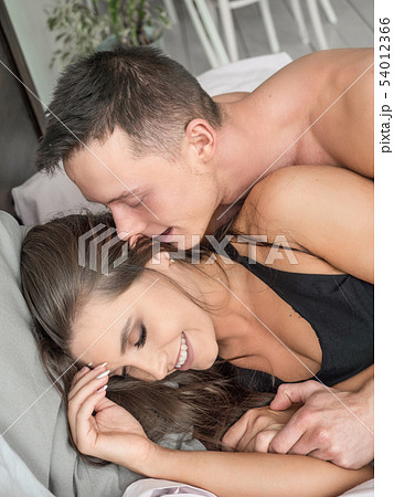 Handsome man kissing woman on cheek early in the morning in the bed. Happy young couple lying down Handsome man kissing woman on cheek early in the morning in the bed. Happy young couple lying down 54012366