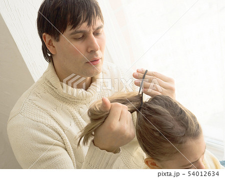 Father with daughter, styling her hair, riding bicycle indoors. 54012634