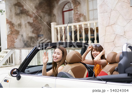高級住宅街に住む友達の家までオープンカーで送り笑顔で手を振ってバイバイして別れる可愛い女性二人の写真素材