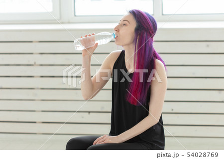 Cute slender young asian woman with colored hair drinking water after gym workout. Concept of 54028769