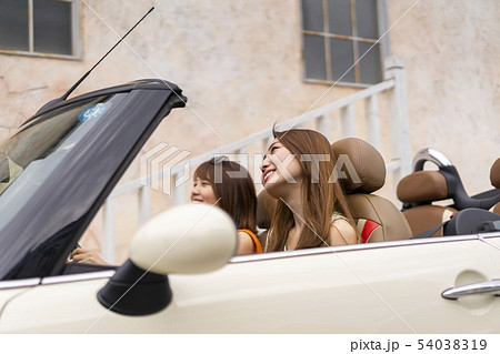 おしゃれな街でオープンカーに乗り気持のいいそよ風で気分も上がる女子旅中の可愛い女性二人の写真素材