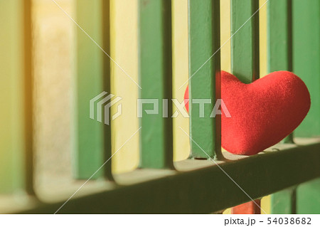 A little red heart pillow on a green steel fence. 54038682