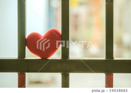 A little red heart pillow on a green steel fence. 54038683