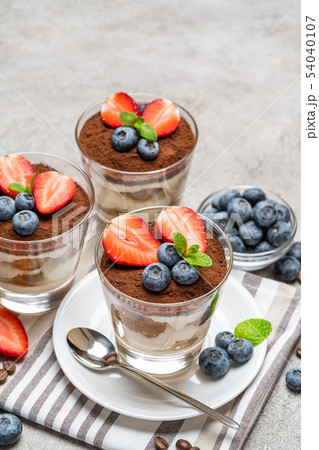 Classic tiramisu dessert with blueberries and strawberries in a glass on concrete background Classic tiramisu dessert with blueberries and strawberries in a glass on concrete background 54040107