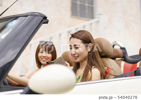 女子旅でオープンカーに乗りおしゃれなカフェをスマホで検索するドライブ中の可愛い女性二人 54040276