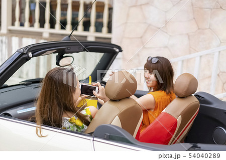 おしゃれな街のカフェでオープンカーに乗り気分も上がりインスタ映えする写真を撮り合う女子旅の女性二人 54040289
