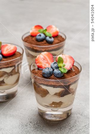 Classic tiramisu dessert with blueberries and strawberries in a glass on concrete background 54041004
