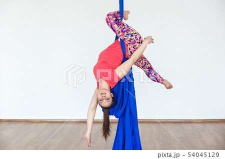 Young girl gymnast hanging on the canvases of cloth in the dance Studio in front of a white wall. 54045129