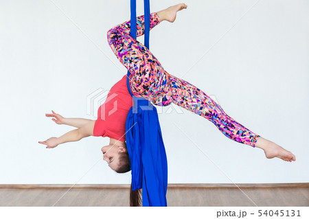 Young girl gymnast hanging on the canvases of cloth in the dance Studio in front of a white wall. 54045131