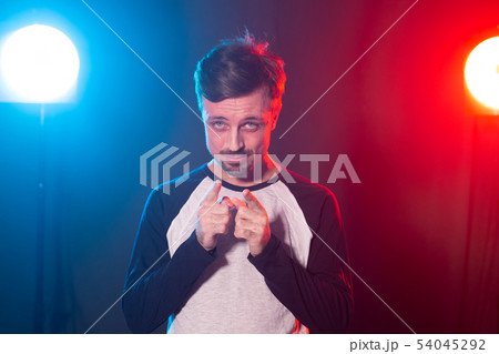Positive handsome young bearded hipster man posing on blue-red background and showing finger at 54045292