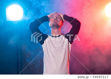 Young slim bearded hipster man with hands on his head and looking up posing on a red-blue background 54045317
