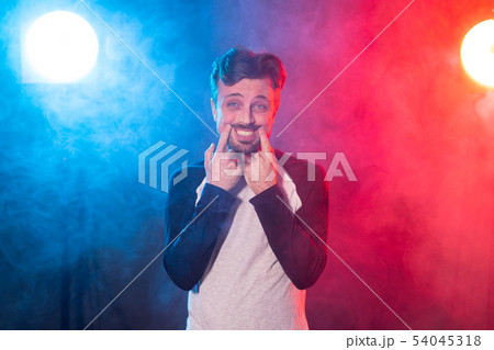 Funny young man with a beard in casual clothes pulls a smile with his hands posing on a red blue 54045318