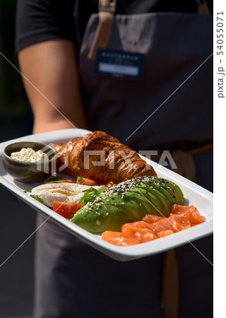 Breakfast is set. Whole grain sandwich with fried egg, red fish, avocado. Plate in the hands of a 54055071