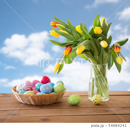 colored easter eggs in basket and flowers over sky colored easter eggs in basket and flowers over sky 54064241