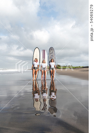 Girls surfers stand with boards on the beach. 54069279