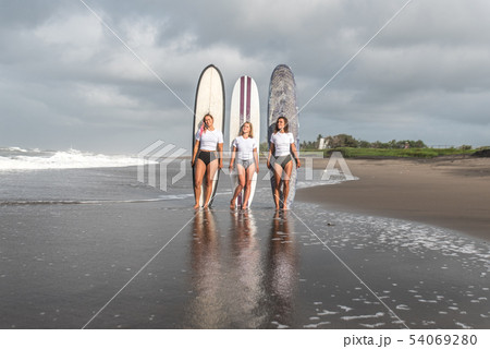 Girls surfers stand with boards on the beach. 54069280
