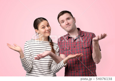 Uncertain couple shrugging shoulders isolated over pink background Uncertain couple shrugging shoulders isolated over pink background 54076138