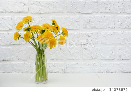 Bouquet of yellow dandelion in vase on table background white brick wall Copy space Minimal style Bouquet of yellow dandelion in vase on table background white brick wall Copy space Minimal style 54078672